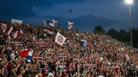 vibrant crowd atmosphere at a nighttime soccer match with fans expressing passion through flags and scarves in the stands under a dusky sky