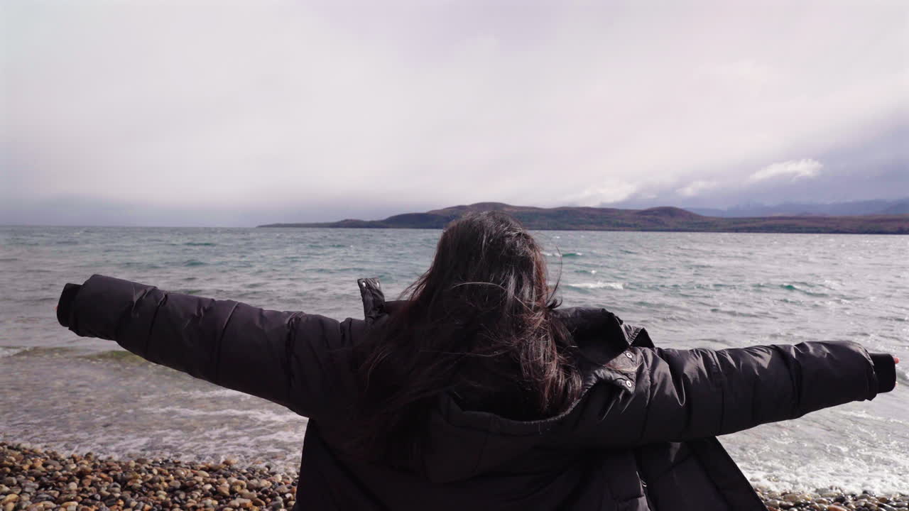Rear view of woman with outstretched arms feeling free, by cold lake in Bariloche, Argentina