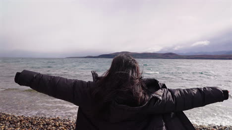 rear view of woman with outstretched arms feeling free, by cold lake in bariloche, argentina