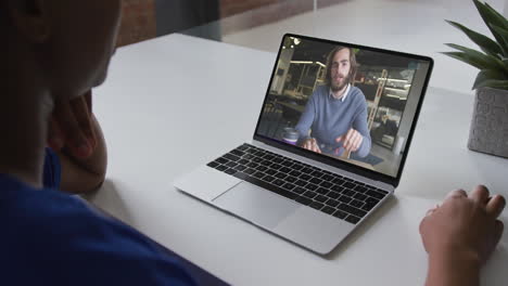 sección media de una mujer afroamericana haciendo una videollamada en una computadora portátil con un colega masculino en la oficina
