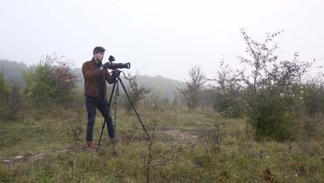 fotógrafo ajustando un trípode con una cámara dslr en un campo brumoso