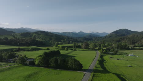 drone shot ascending over lush green fields with mountains and hills in the distance, new zealand