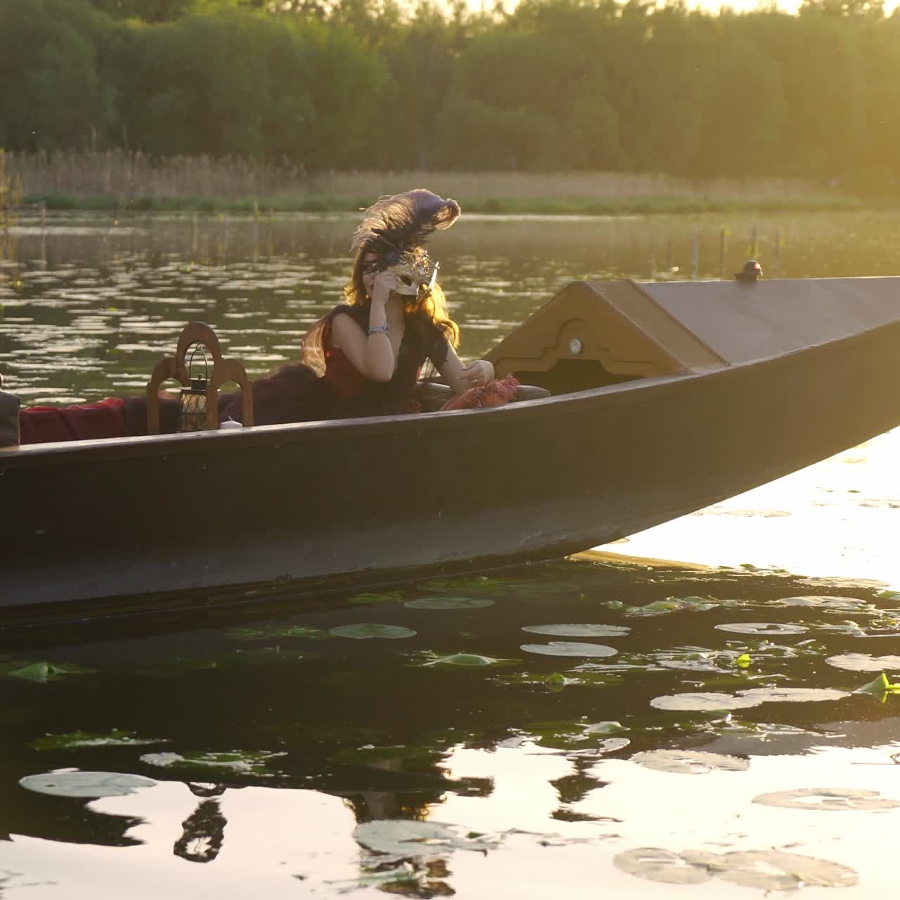 Bella donna in abito è su una gondola e sta indossando una maschera di carnevale sul fiume.