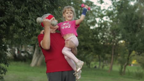 granddaughter and grandfather doing fitness exercises with dumbbells. senior man with child kid girl