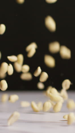 vertical video close up shot of peanuts dropping onto marble surface shot in slow motion