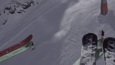 Ascent-in-chairlift,-skis-placed-on-a-base,-ski-slope-and-skiers-descending-the-ski-slope-below,-Swiss-Alps,-Zermatt,-snow-capped-mountains