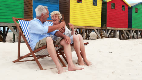 senior couple toasting drinks near colorful beach hut