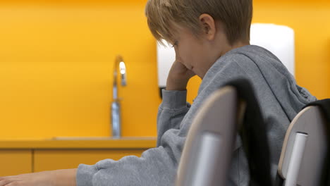 Isolated-school-boy-with-tablet-sitting-at-desk-in-class,-raising-hand,-static-side-shot