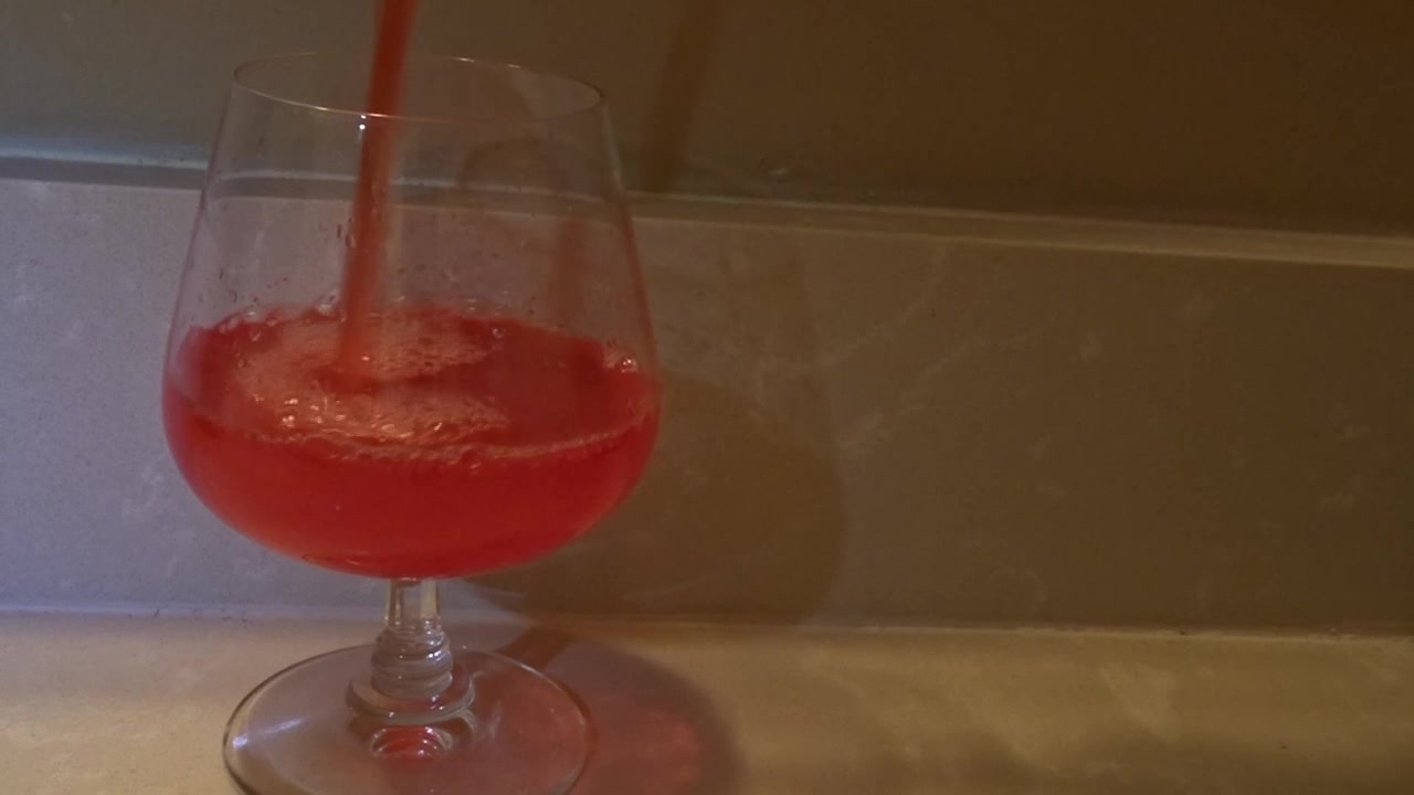 Tomada frontal de líquido vermelho sendo derramado em taça de vinho