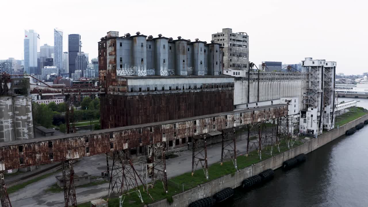 Aerial view of rusted industrial silos with a modern city skyline backdrop. A stunning contrast of urban decay and sleek architecture. Montreal's Old Port docks.