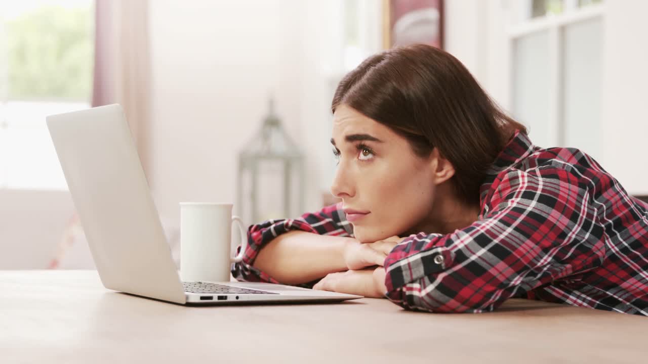 mujer agotada usando una computadora portátil mientras bebe café