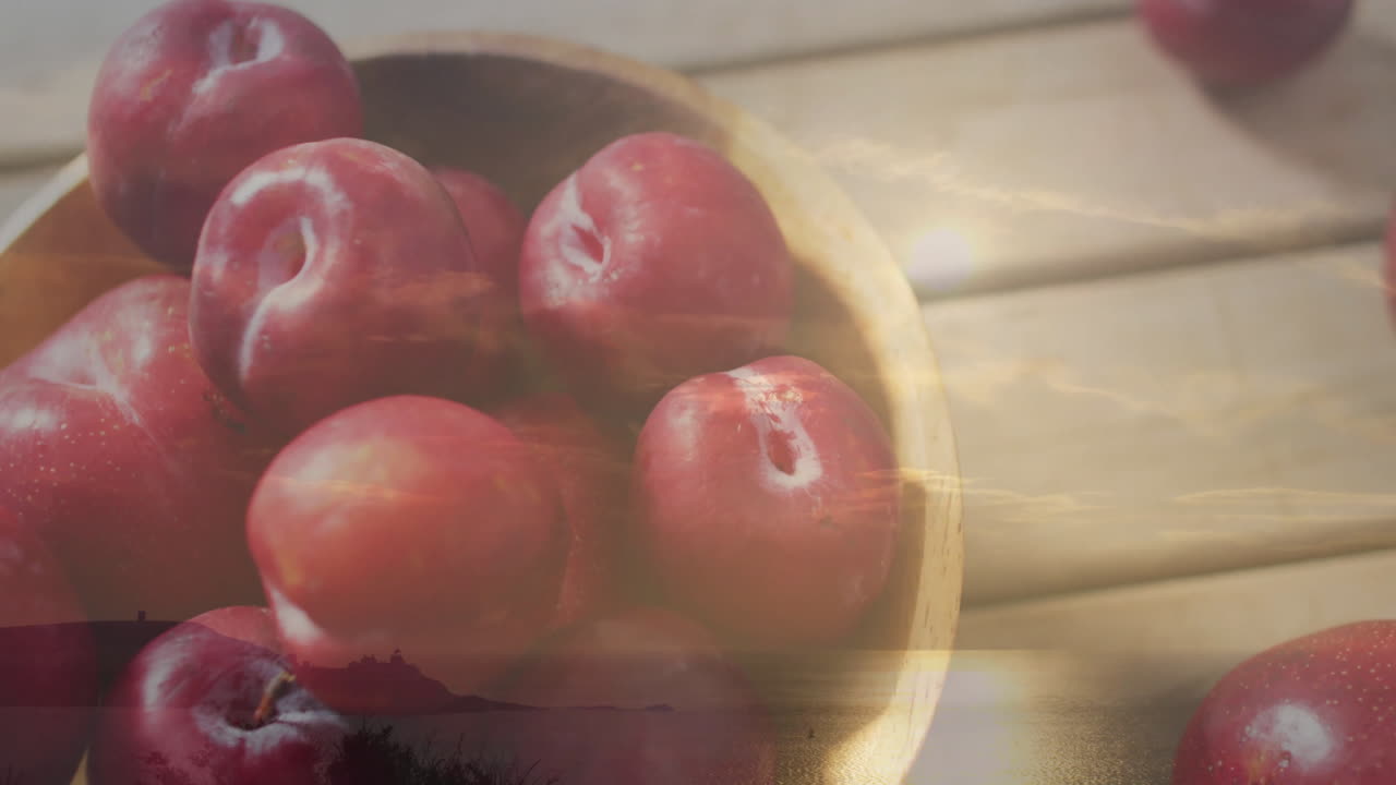 Red plums in bowl over calm water at sunset, creating serene landscape