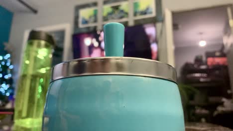 young adult male hand a marijuana cigarette into a light blue ashtray inside a small house with the television playing in the background