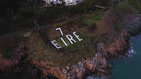 eire 7, world war ii coastal watch marker sign, killiney, dublin, ireland. january 2020. drone descends gradually revealing people exercising, walking dogs and swimmers at base of the coastal cliffs