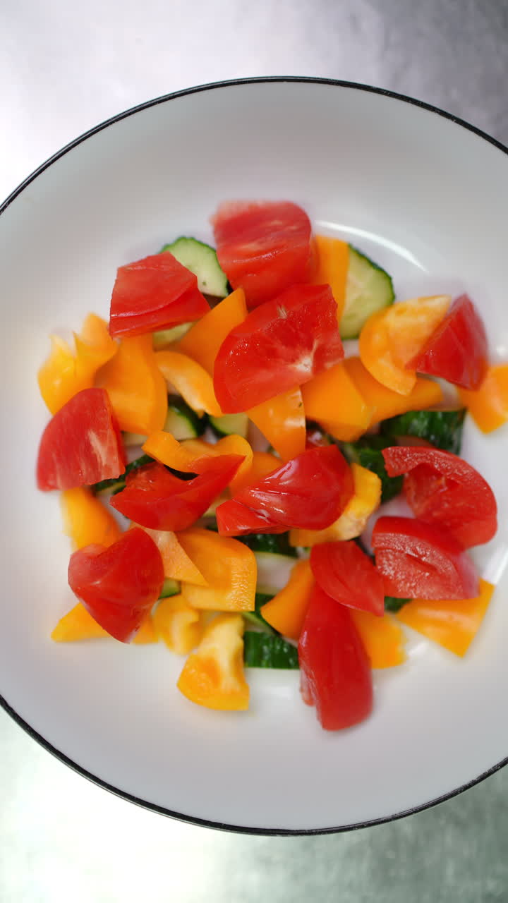 Vertical footage Professional chef sprinkling salt, seasoning colorful salad featuring ripe tomatoes, crisp cucumbers, vibrant yellow bell peppers