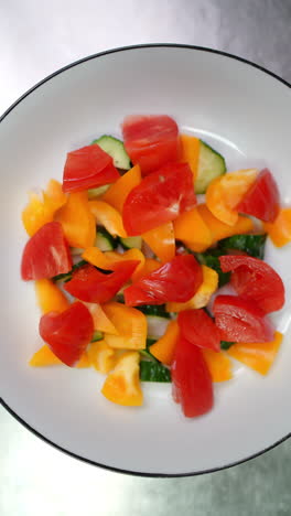 vertical footage professional chef sprinkling salt, seasoning colorful salad featuring ripe tomatoes, crisp cucumbers, vibrant yellow bell peppers