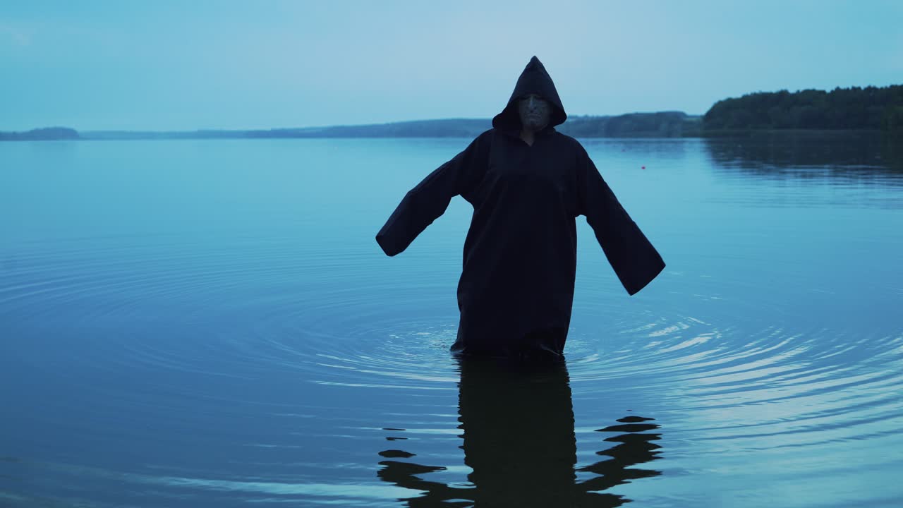 Evil witch in black cloak with hood in the river. Halloween costume.