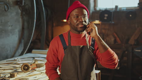 blacksmith talking on mobile phone in metalworking workshop