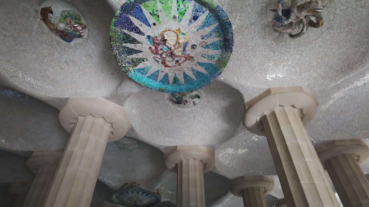Mosaic art on the ceiling of the Hypostyle Room in Park Güell, showcasing intricate designs and vibrant colors celebrated for their unique aesthetic and historical significance.