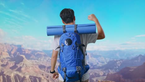 back view of a male hiker with mountaineering backpack screaming goal celebrating the success while traveling at the top of mountain