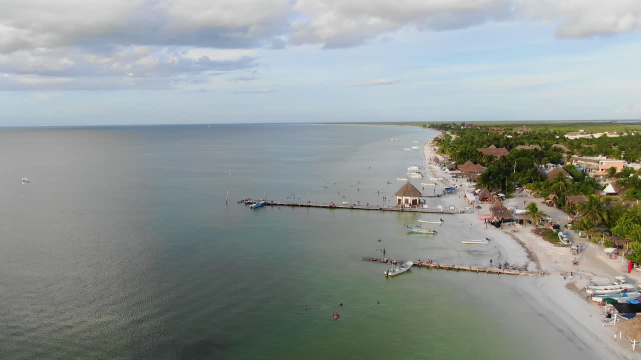 Aerial view Move away shot, scenic view pump boats and people on the shoreline of Isla Holbox, Mexico, green beach, palm tree and houses in the background