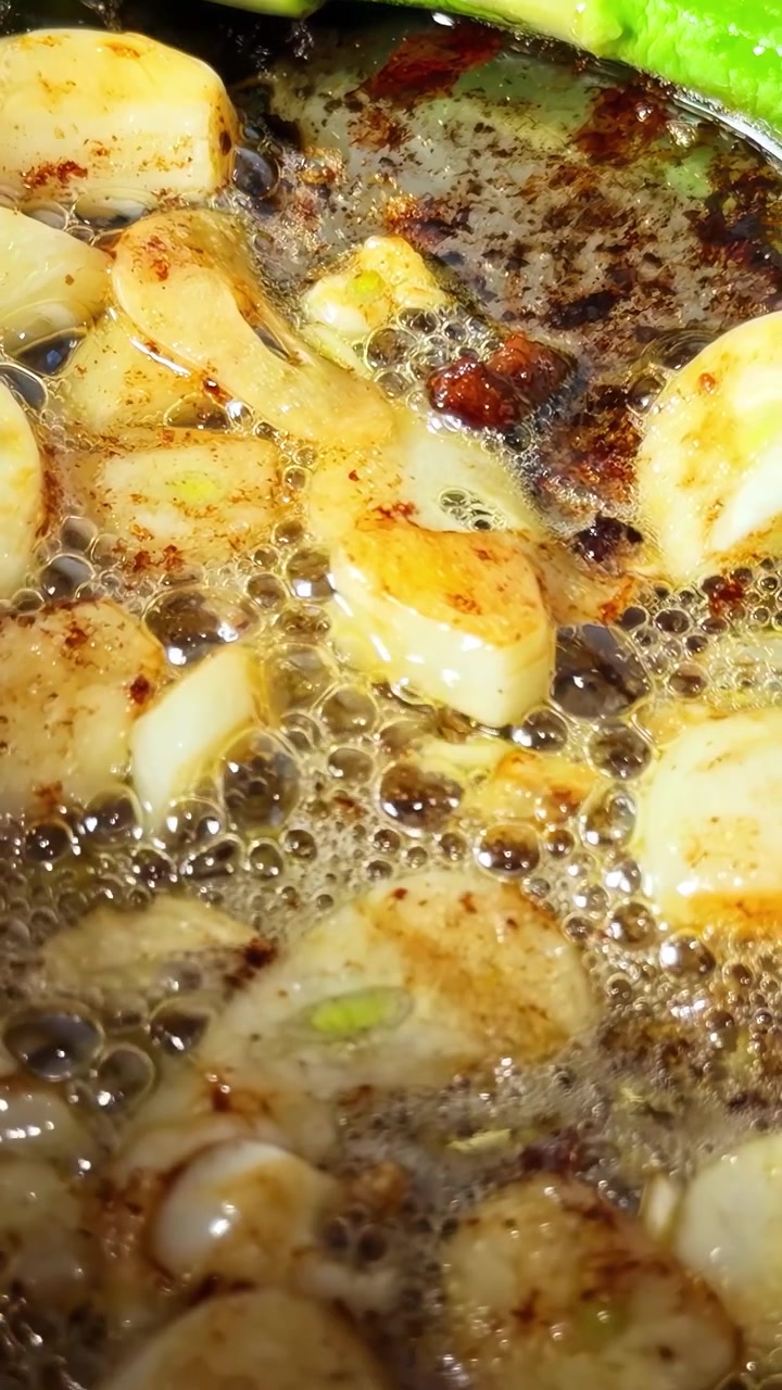 Ekstremt nærbillede af gyldne kammuslinger, der syder i mørkt boblende smør med levende grønne asparges, hvilket fanger præcisionen i gourmetmadlavning
