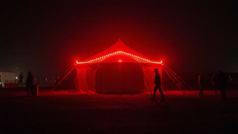 an enigmatic red tent illuminates the night, drawing curiosity and intrigue from passersby and creating a mysterious atmosphere in the dark