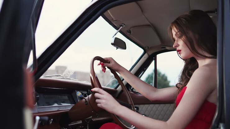 Donna alla guida di un'auto d'epoca in abito rosso