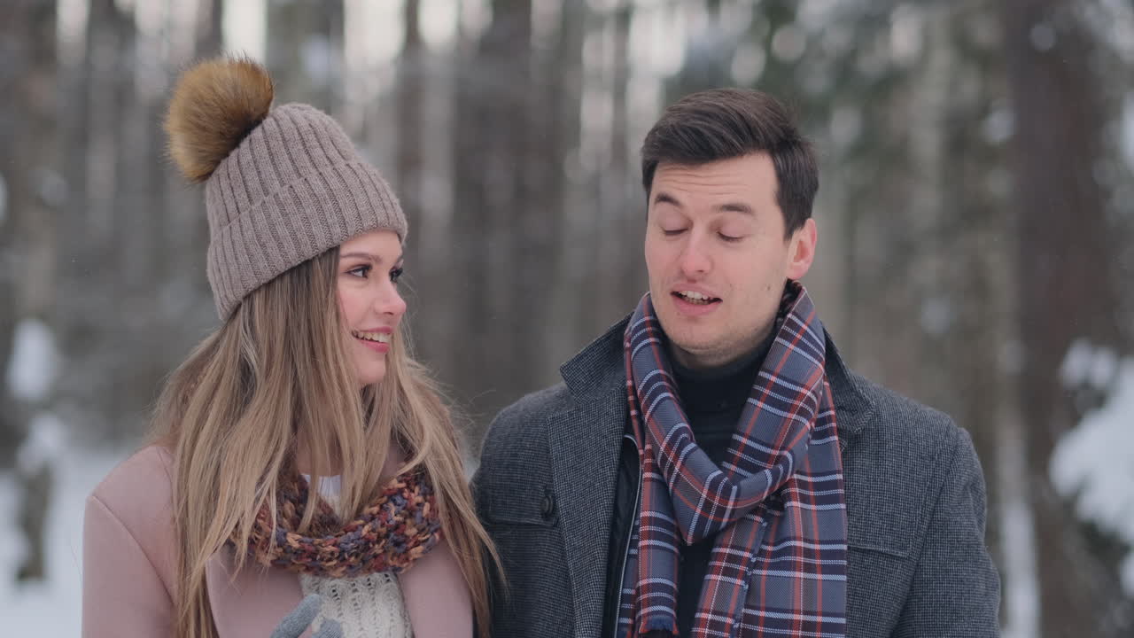 A young man and a woman in a coat are having fun and playing with snow in a winter forest in slow motion. Happiness and smiles on faces
