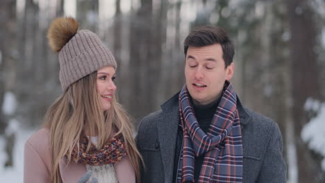 a young man and a woman in a coat are having fun and playing with snow in a winter forest in slow motion. happiness and smiles on faces