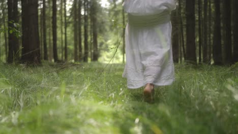 woman with bare feet is walking in the green grass in the forest on a sunny day. relax in nature, slow motion
