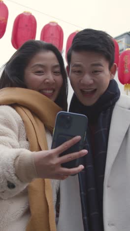 Video-Vertical-De-Una-Joven-Pareja-Asiática-De-Vacaciones-Posando-Para-Un-Selfie-En-Un-Teléfono-Móvil-En-Chinatown,-Londres,-Reino-Unido