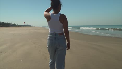 woman walking on the beach in jeans and a shirt, looking to the horizon