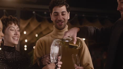 hombre feliz sirviendo champán en las copas de sus alegres amigos en la fiesta de fin de año