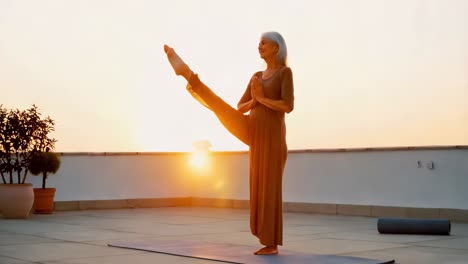 senior woman practicing yoga on rooftop at sunrise