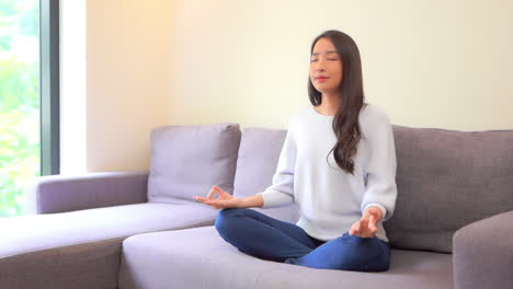 a lovely young woman sitting cross-legged strikes a yoga pose as she meditates