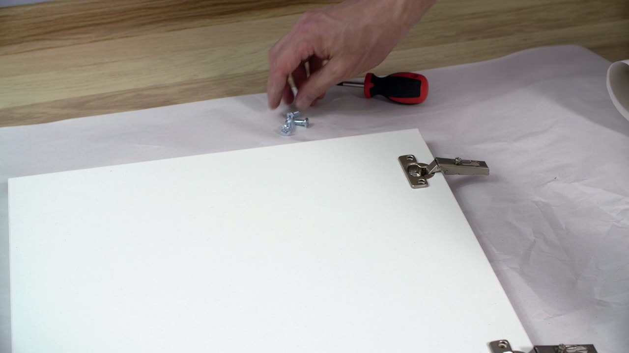 Male hand fixing screw with screwdriver on furniture loop while assembly. Carpenter collecting hinge on office furniture door. Craftsman assembling kitchen furniture.