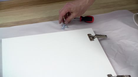 male hand fixing screw with screwdriver on furniture loop while assembly. carpenter collecting hinge on office furniture door. craftsman assembling kitchen furniture.