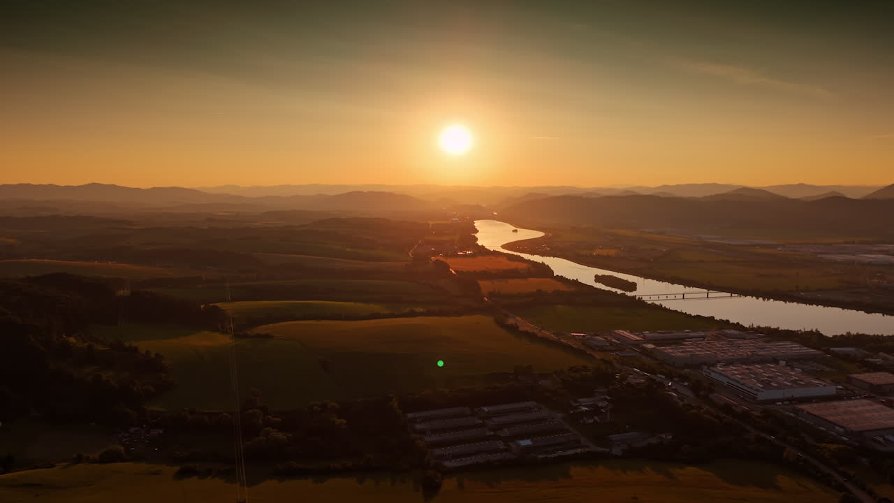 Flight over the vast countryside dazzled by orange light of sunset. Silhouettes of the Tatra mountains at backdrop