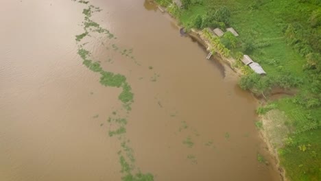 Pequeña-Canoa-Indígena-En-El-Río-Orinoco-Y-Un-Pequeño-Pueblo-Indígena-En-La-Orilla