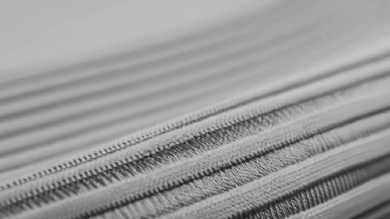 Makro pohled na pletené textilní šňůry uspořádané diagonálně, s ostrými detaily v popředí, pevně pletenými smyčkami, žebrovanou strukturou, vrstvenými prameny, měkkým směrovým světlem a jemným monochromatickým kontrastem.