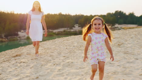 happy childhood mother playing with her daughter on the beach girl laughs and runs away from his mot