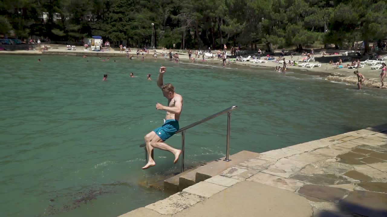 Giovane uomo europeo biondo e atletico che scivola su un corrimano affacciato sul mare, con effetto speed ramp e slow motion.