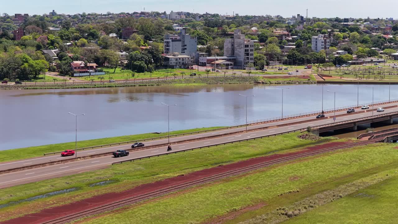 Vehicles cross over the Paraná River at Acceso Sur, with Posadas city and green riverbanks in Misiones, Argentina visible beyond