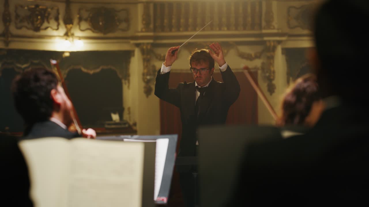 Cinematic shot of conductor directing symphony orchestra with performers playing violins, cello and trumpet