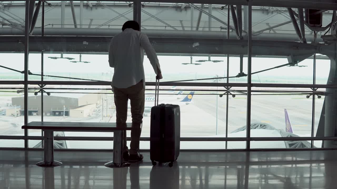 4K. Male Young passenger using smartphone walking with suitcase luggage and sitting on bench in departure area of airport terminal. Asian businessman on business trip. Modern travel lifestyle concepts