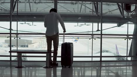 4k. male young passenger using smartphone walking with suitcase luggage and sitting on bench in departure area of airport terminal. asian businessman on business trip. modern travel lifestyle concepts