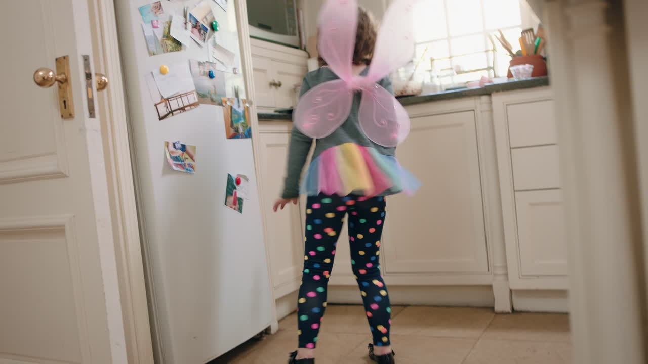 una niña feliz bailando en la cocina con adorables alas de hada divirtiéndose agitando una cuchara jugando a fingir haciendo movimientos de baile divertidos disfrutando del fin de semana en casa