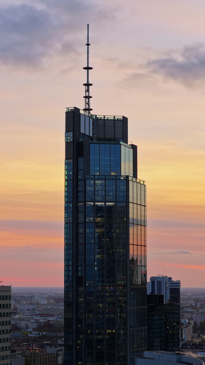 Aerial drone view of the Warsaw Trade Tower featuring its rooftop antenna, set against an overcast evening sky in Warsaw's Wola district. Vertical