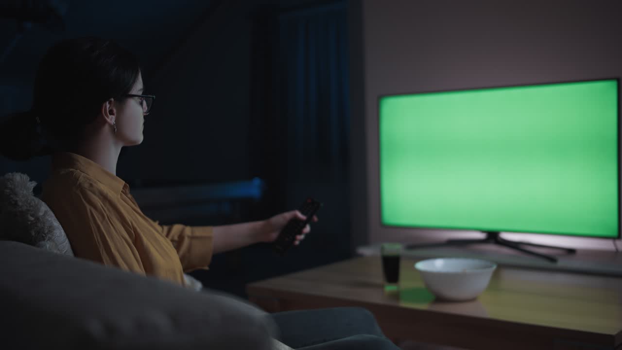 chroma key, scatto cinematografico, una ragazza adolescente è seduta sul divano a casa la sera, guardando la tv e cambiando canale